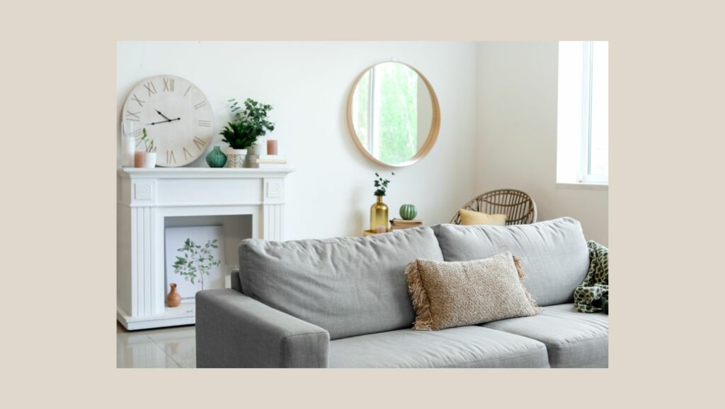Sala de estar aconchegante com espelho redondo na parede, sofá cinza e elementos decorativos em tons claros.